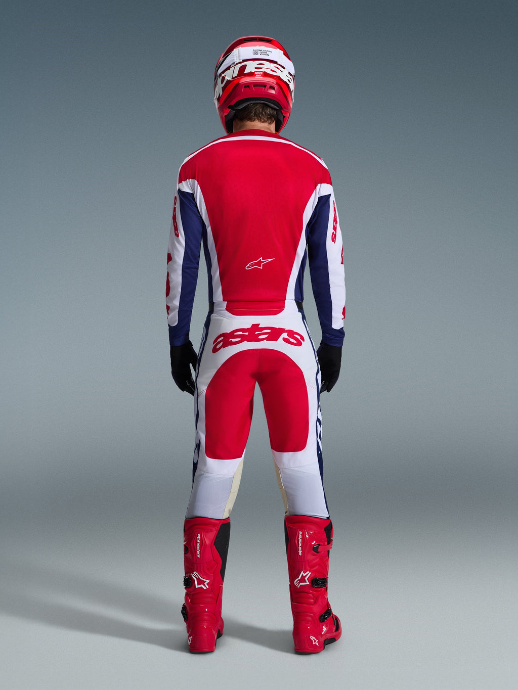 Motocross-Fahrer in kompletter Rennausrüstung von hinten, Alpinestars 2026 Racer Riway Jersey in Weiß-Blau-Rot, passende weiß-rote Hose mit markantem 'astars'-Branding, rote Stiefel und rot-weißer Helm, abgestimmtes Offroad-Rennoutfit.