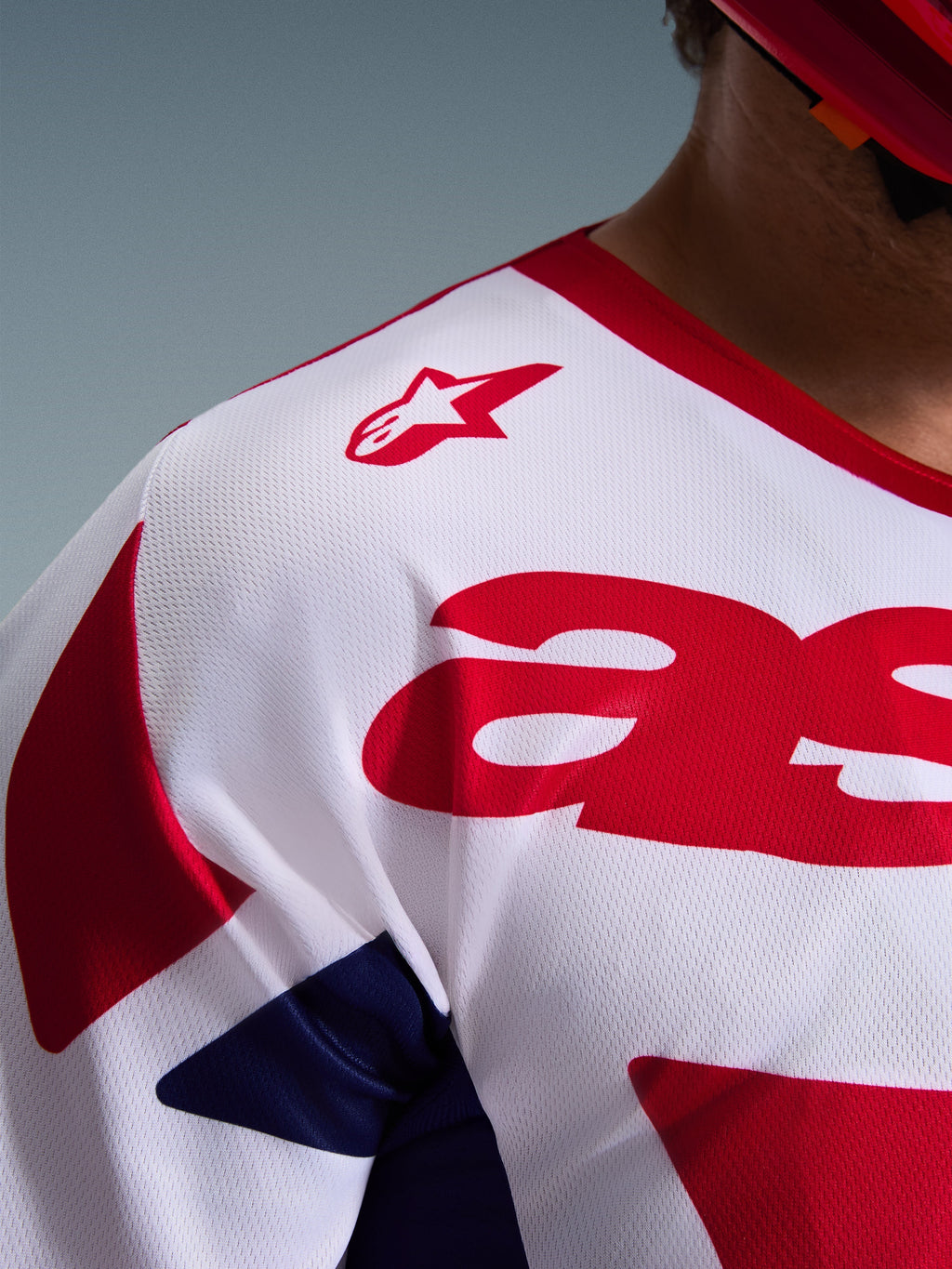 Nahaufnahme des Alpinestars 2026 Racer Riway Trikots, Motocross-Trikot in Weiß, Blau und Rot, mit atmungsaktiver, feuchtigkeitsableitender Mesh-Struktur, rotem Stern-Logo auf der Schulter und markanten roten Grafiken auf der Brust