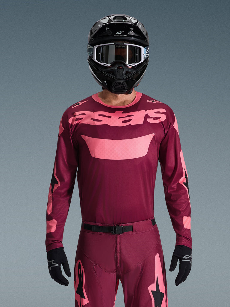 Motocross-Fahrer im Alpinestars 2026 Racer Riway Trikot in Dark Red Coral, mit weinrotem Hauptteil und 'astars'-Branding in Korallenrosa auf der Brust, kombiniert mit passender Motocross-Hose, schwarzem Helm und schwarzen Handschuhen, professionelles Ausrüstungsset für Offroad-Rennen.