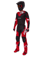 Motocross-Fahrer in kompletter Rennausrüstung mit dem Alpinestars 2025 Racer Veil Trikot in Schwarz und Bright Red, passender Hose, roten Stiefeln, schwarzem Helm mit roter Brille und rot-schwarzen Handschuhen, abgestimmter Performance-Look für den Offroad-Rennsport