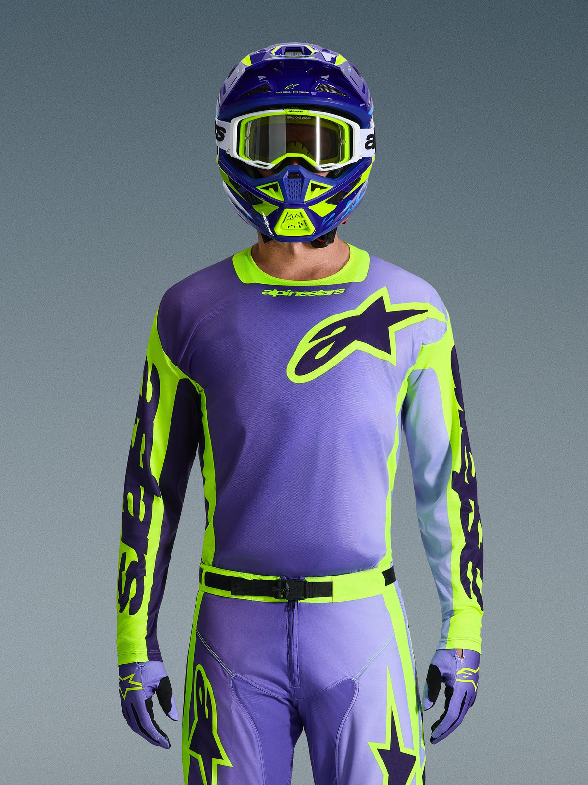 Alpinestars 2026 Racer Portl Jersey, Motocross Jersey, Purple and Yellow Fluo, worn with matching motocross pants, gloves, and helmet, featuring a large Alpinestars star logo on the chest, studio shot against a gray background.