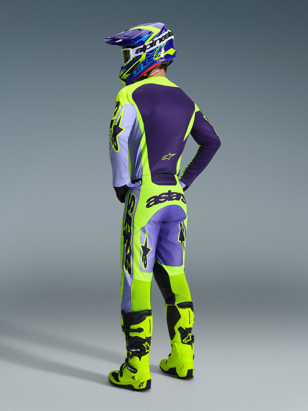 Motocross rider wearing Alpinestars 2026 Racer Portl Jersey and pants, Purple and Yellow Fluo gear set, back view featuring matching helmet and neon yellow boots, coordinated professional off-road racing outfit.