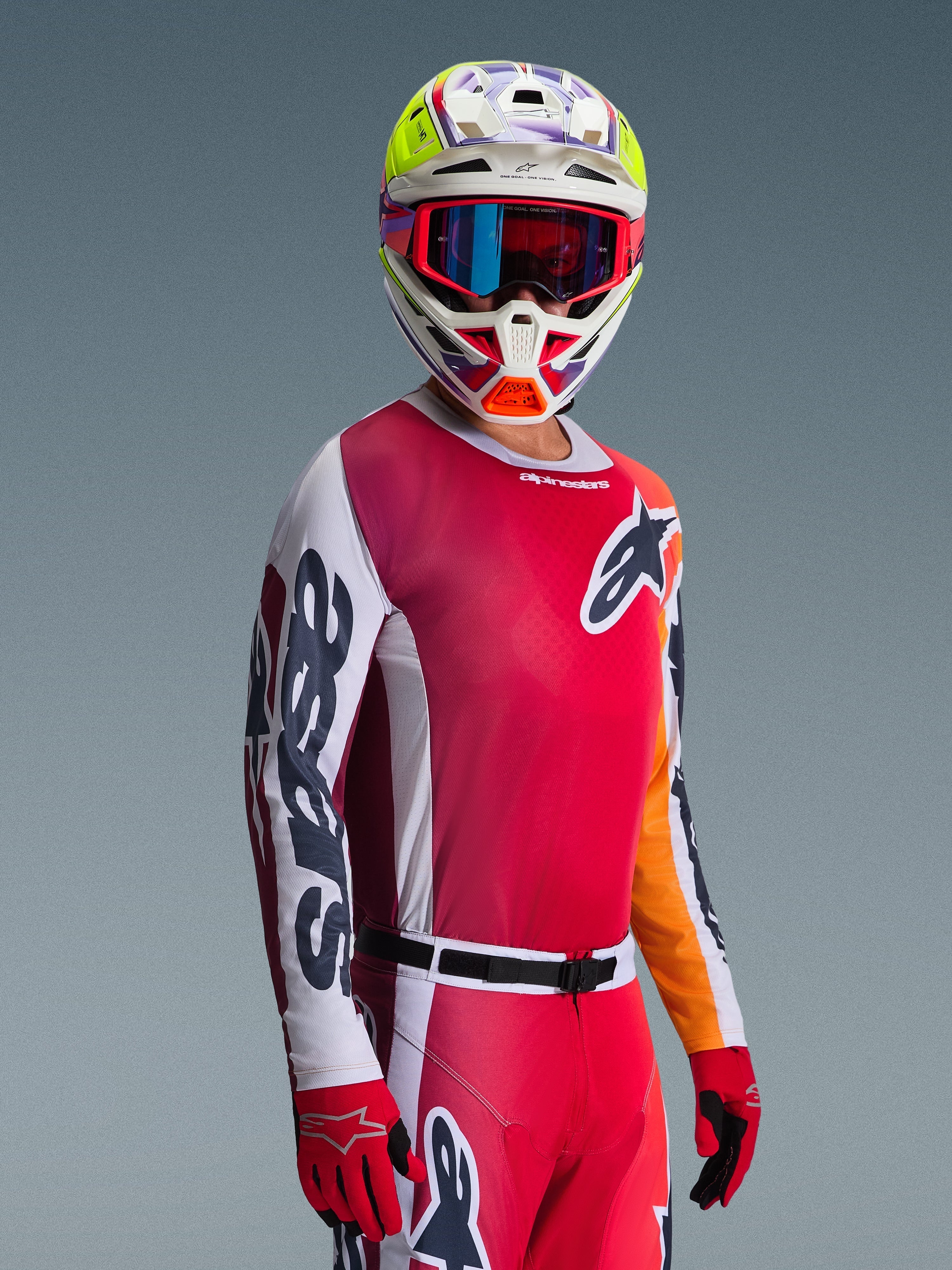 Motocross rider wearing the 2026 Racer Portl Jersey, Red with white and dark gray sleeves, paired with matching motocross pants, multi-colored helmet with blue goggles, and red gloves, studio shot