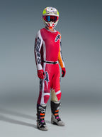 Motocross rider wearing complete racing gear, Alpinestars 2026 Racer Portl Jersey in red and light gray, matching motocross pants with white and dark green accents, multi-colored helmet with red goggles, gray and black boots with orange and purple details, red gloves, coordinated outfit for off-road racing