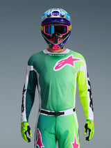Alpinestars 2026 Racer Portl Jersey, Motocross Jersey, Green White and Black with a large pink Alpinestars logo on the chest, worn by a rider with a vibrant multi-colored helmet and matching goggles, professional off-road racing apparel.