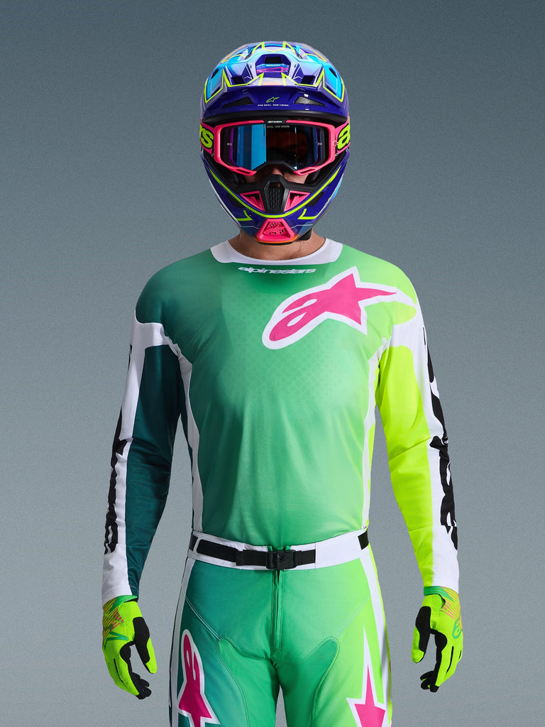 Alpinestars 2026 Racer Portl Trikot, Motocross-Trikot, Grün, Weiß und Schwarz mit einem großen pinkfarbenen Alpinestars-Logo auf der Brust, getragen von einem Fahrer mit einem auffälligen mehrfarbigen Helm und passender Brille, professionelle Offroad-Rennbekleidung