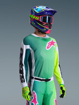 Alpinestars 2026 Racer Portl Jersey, Motocross Jersey, Green White and Black, worn by a rider with matching green pants, fluorescent gloves, and a vibrant blue and purple helmet with pink goggles, featuring a pink Astars logo on the chest.