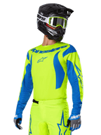 Alpinestars 2025 Fluid Haul Ausrüstungsset, Motocross-Trikot und -Hose, leuchtendes Gelb und Blau, getragen mit schwarzem Helm und gelber Crossbrille, wellenartige blaue Muster an den Ärmeln und blaue Stern-Logos auf der Hose, abgestimmtes Offroad-Rennoutfit