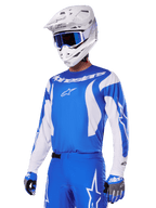 Motocross-Fahrer im Alpinestars 2025 Fluid Haul Gear Set in Blau und Weiß, bestehend aus einem blauen Jersey mit weißen Akzenten, passender blauer Hose mit Stern-Logos, weißem Helm mit blauer Goggle und abgestimmten blau-grauen Handschuhen, komplette Offroad-Rennausrüstung.