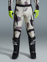 Alpinestars 2026 Racer Lahnd Hose, Motocross-Hose, Sand-Camo-Muster mit grauen und lila abstrakten Grafiken, getragen mit neongelben Handschuhen und schwarzen Stiefeln, schwarze Stern-Logos auf den Oberschenkeln und ein schwarzer Taillengürtel, strapazierfähige Offroad-Rennausrüstung
