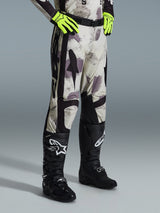 Alpinestars 2026 Racer Lahnd Hose, Motocross-Hose, Sand Camo, kombiniert mit neongelben Handschuhen und schwarzen Motocross-Stiefeln, mit abstraktem Camouflage-Muster und schwarzen Seiteneinsätzen, ergonomisches Offroad-Design