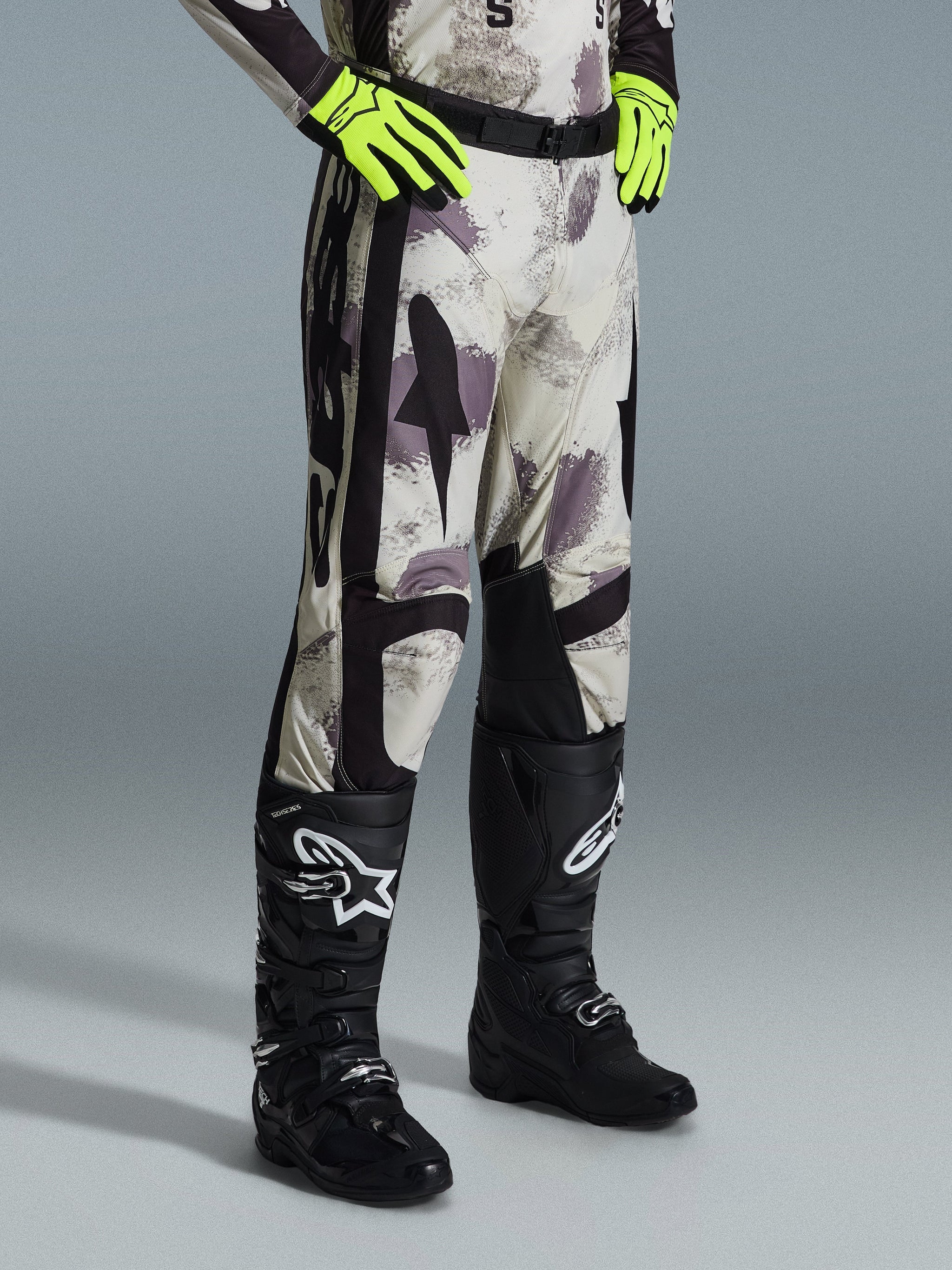 Alpinestars 2026 Racer Lahnd Hose, Motocross-Hose, Sand Camo, kombiniert mit neongelben Handschuhen und schwarzen Motocross-Stiefeln, mit abstraktem Camouflage-Muster und schwarzen Seiteneinsätzen, ergonomisches Offroad-Design