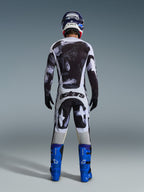 Motocross-Fahrer in der Rückansicht im Alpinestars 2026 Racer Lahnd Gear Set, schwarz-weiß abstrakt gemustertes Jersey und Hose, „astars“-Branding auf dem Gesäß, kombiniert mit blauen Stiefeln und passendem Helm, professionelle Offroad-Rennbekleidung.