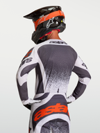 Alpinestars Techstar Swan Trikot, athletisches Motocross-Jersey in Dunkelgrau und Weiß mit roten Details, am Fahrer in Rückenansicht gezeigt.