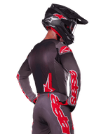 Alpinestars 2025 Supertech Lipan Ausrüstungsset, Rückansicht eines Motocross-Fahrers, anthrazitgraues Trikot und Hose mit leuchtend rotem 'astars'-Branding auf den Ärmeln und dem Rücken, kombiniert mit einem schwarzen Helm
