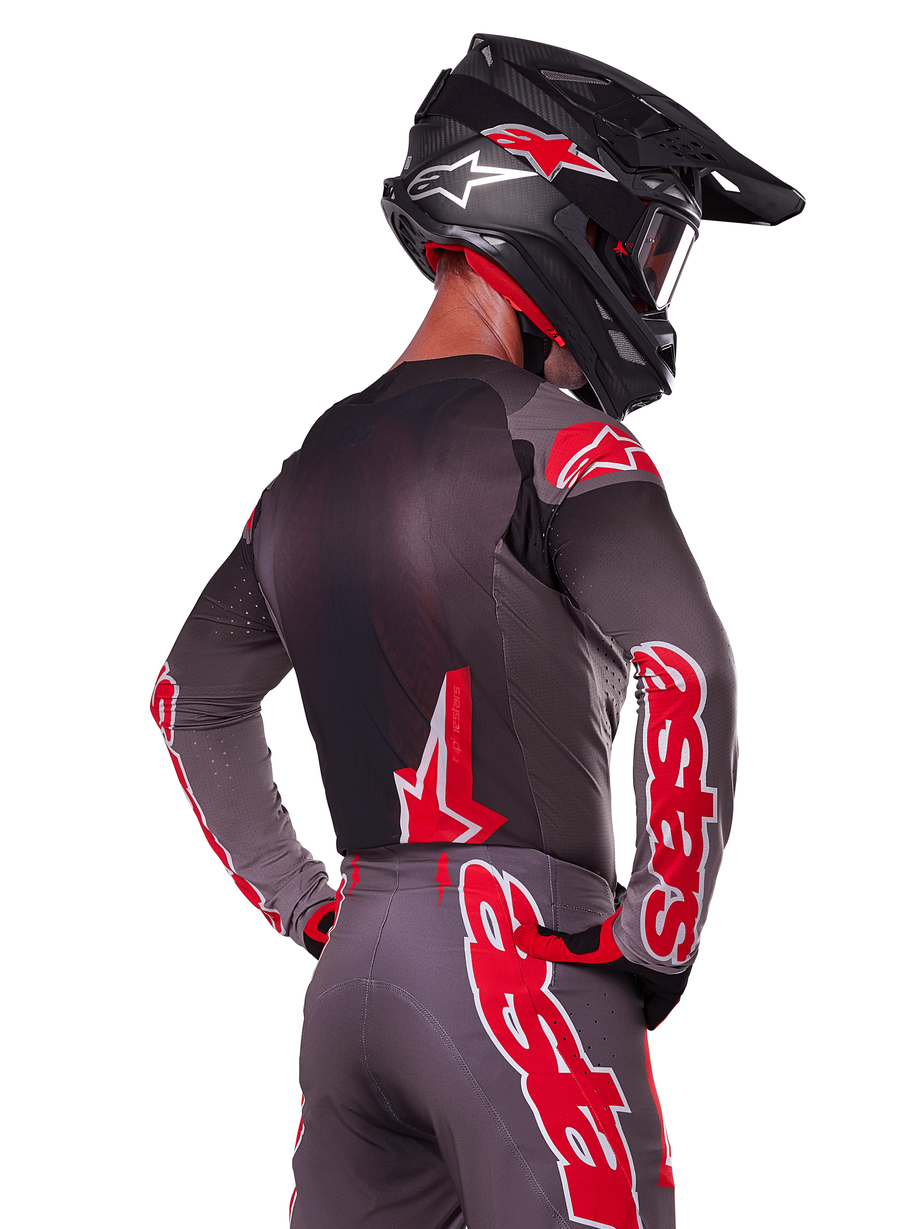 Alpinestars 2025 Supertech Lipan Ausrüstungsset, Rückansicht eines Motocross-Fahrers, anthrazitgraues Trikot und Hose mit leuchtend rotem 'astars'-Branding auf den Ärmeln und dem Rücken, kombiniert mit einem schwarzen Helm