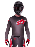 Alpinestars 2025 Supertech Lipan Trikot, Motocross-Jersey, Smoke und Rot, mit einem großen rot-weißen Brustlogo, getragen mit einem schwarzen Helm und rot-schwarzen Handschuhen, athletische Rennpassform mit lasergeschnittenen Perforationen