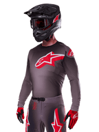 Alpinestars 2025 Supertech Lipan Ausrüstungsset, Motocross-Fahrer in dunkelgrauem Jersey und Hose mit roten und weißen Akzenten, großes rotes Alpinestars-Logo auf der Brust, lasergeschnittene Perforationen zur Belüftung, schwarzer Helm, rote Brille und rot-schwarze Handschuhe