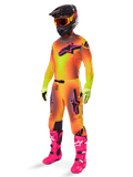 Motocross rider wearing the 2025 Alpinestars Supertech Lipan Gear Set, yellow and orange gradient jersey and pants with pink accents, black helmet with yellow-red goggles, bright yellow gloves, and vibrant pink boots, coordinated off-road racing outfit