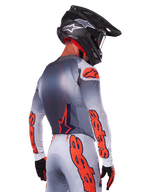 Motocross-Fahrer von hinten im Alpinestars 2025 Supertech Lipan Jersey in Grau Orange Fluo, mit markanten orangefarbenen Logos auf den Ärmeln und dem Rücken, kombiniert mit passender Hose und schwarzem Helm, professionelles Rennoutfit für Offroad-Performance.
