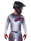 2025 Supertech Lipan Trikot, Motocross-Renntrikot, Grau mit Akzenten in Orange und Marineblau, langärmeliges Performance-Oberteil mit perforierten Belüftungsdetails, getragen mit schwarzem Helm und roten Handschuhen, schnittiges Racing-Design
