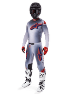Motocross-Fahrer im Alpinestars 2025 Supertech Lipan Jersey in Grau und Orange Fluo, passende graue Hose mit orangefarbenen Akzenten, schwarzer Helm, weiß-schwarze Stiefel und orange-schwarze Handschuhe, professionelles Ausrüstungsset für Offroad-Rennen