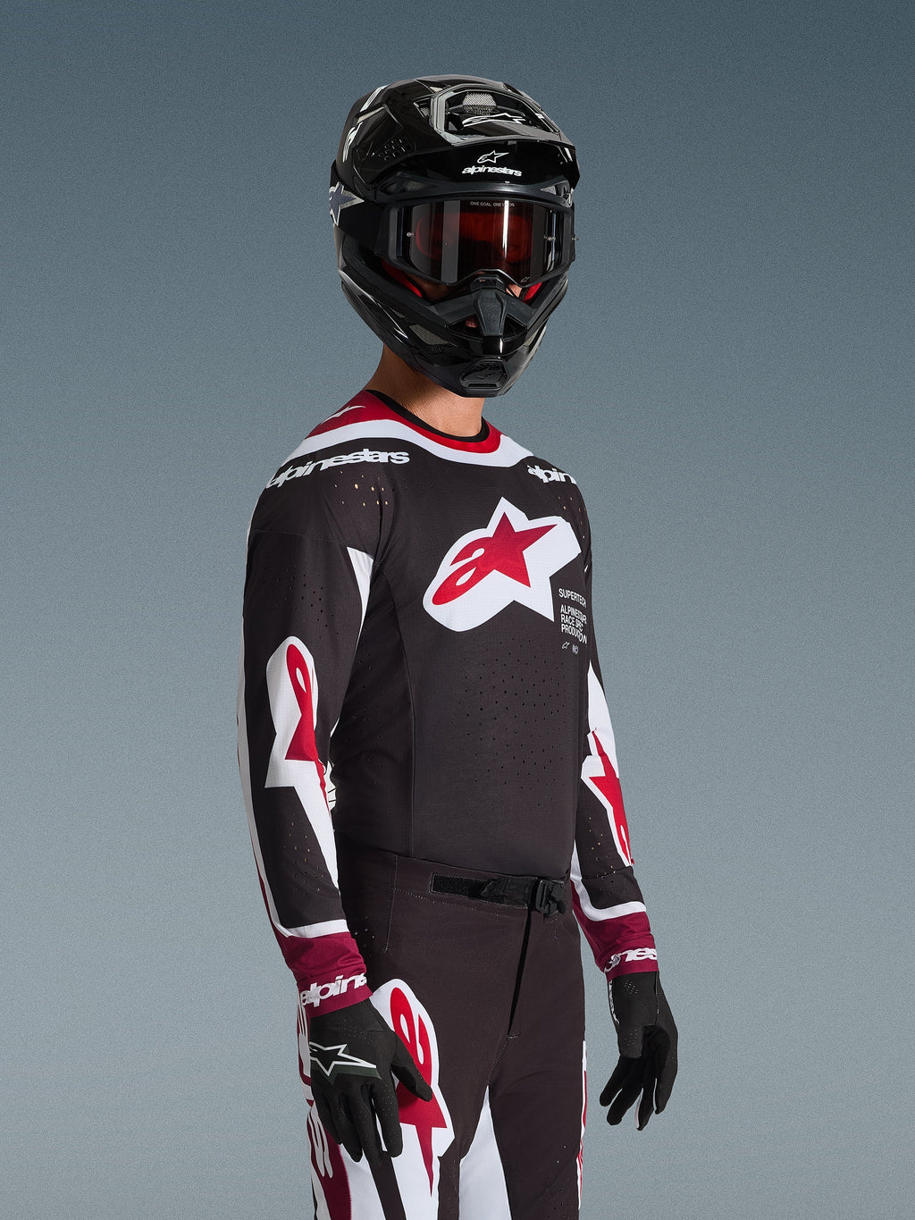 Motocross rider wearing the Alpinestars 2026 Supertech AFD Vista Jersey in Black Red and White, featuring a large red star logo on the chest and laser-cut perforations, paired with a black helmet and matching racing pants for off-road performance