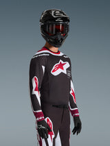 Motocross rider wearing the Alpinestars 2026 Supertech AFD Vista Jersey in Black Red and White, featuring a large red star logo on the chest and laser-cut perforations, paired with a black helmet and matching racing pants for off-road performance
