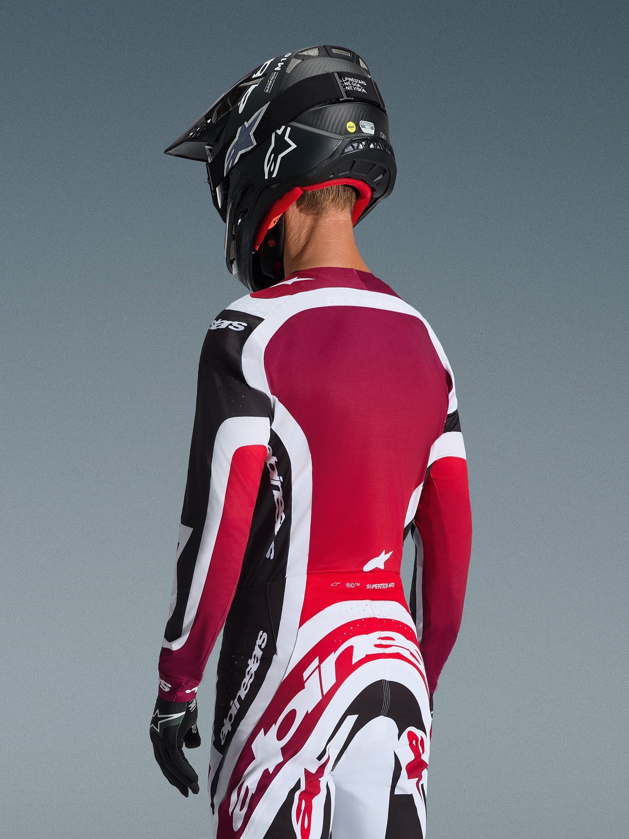 Rear view of a motocross rider wearing the 2026 Supertech AFD Vista Jersey in Black Red and White, coordinated with matching pants and a black helmet, featuring bold Alpinestars branding, red mesh panels, and an athletic racing fit.