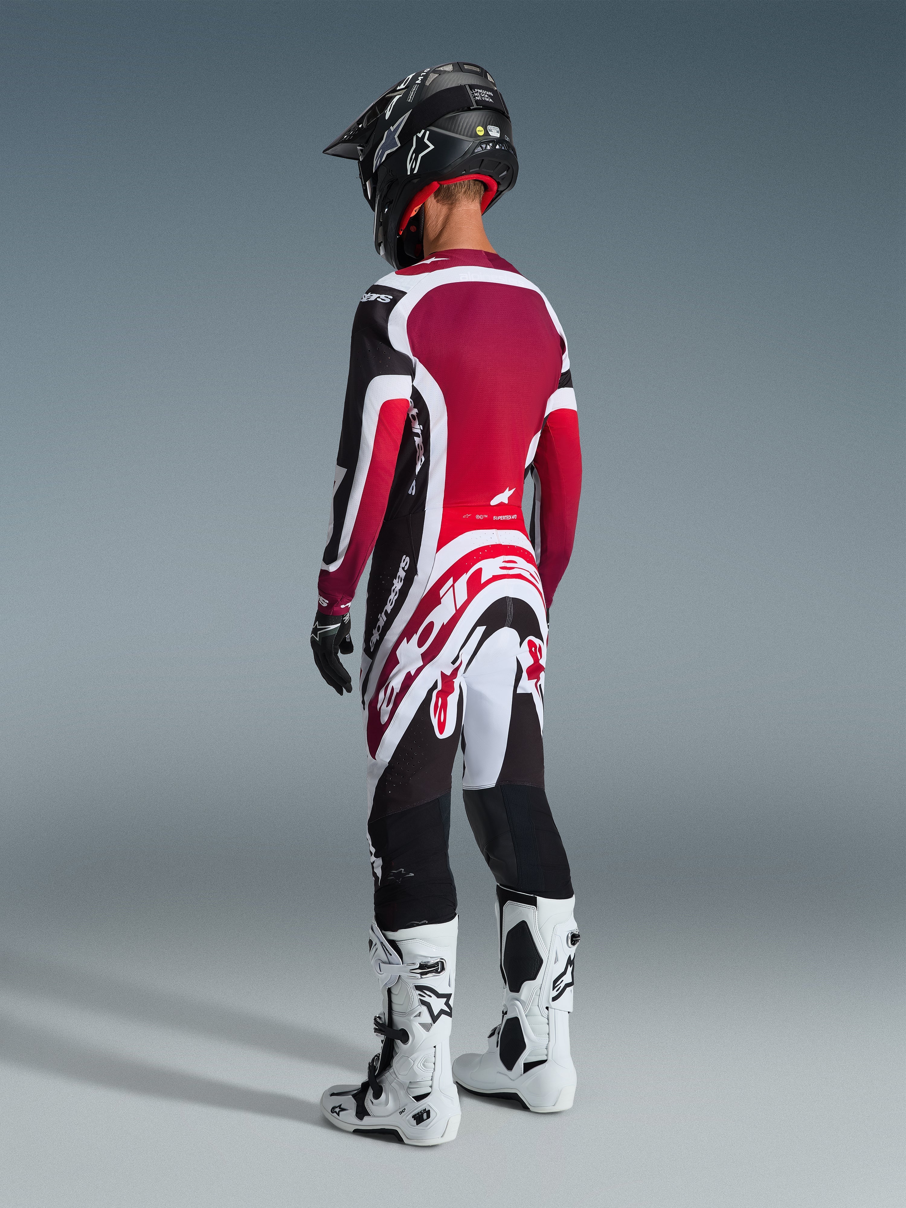 Motocross-Fahrer in der Rückansicht, trägt das Alpinestars 2026 Supertech AFD Vista Gear Set, rot-weiß-schwarzes Trikot und Hose mit markantem Alpinestars-Branding, schwarzer Helm, weiß-schwarze Stiefel und schwarze Handschuhe für einen kompletten professionellen Rennlook.