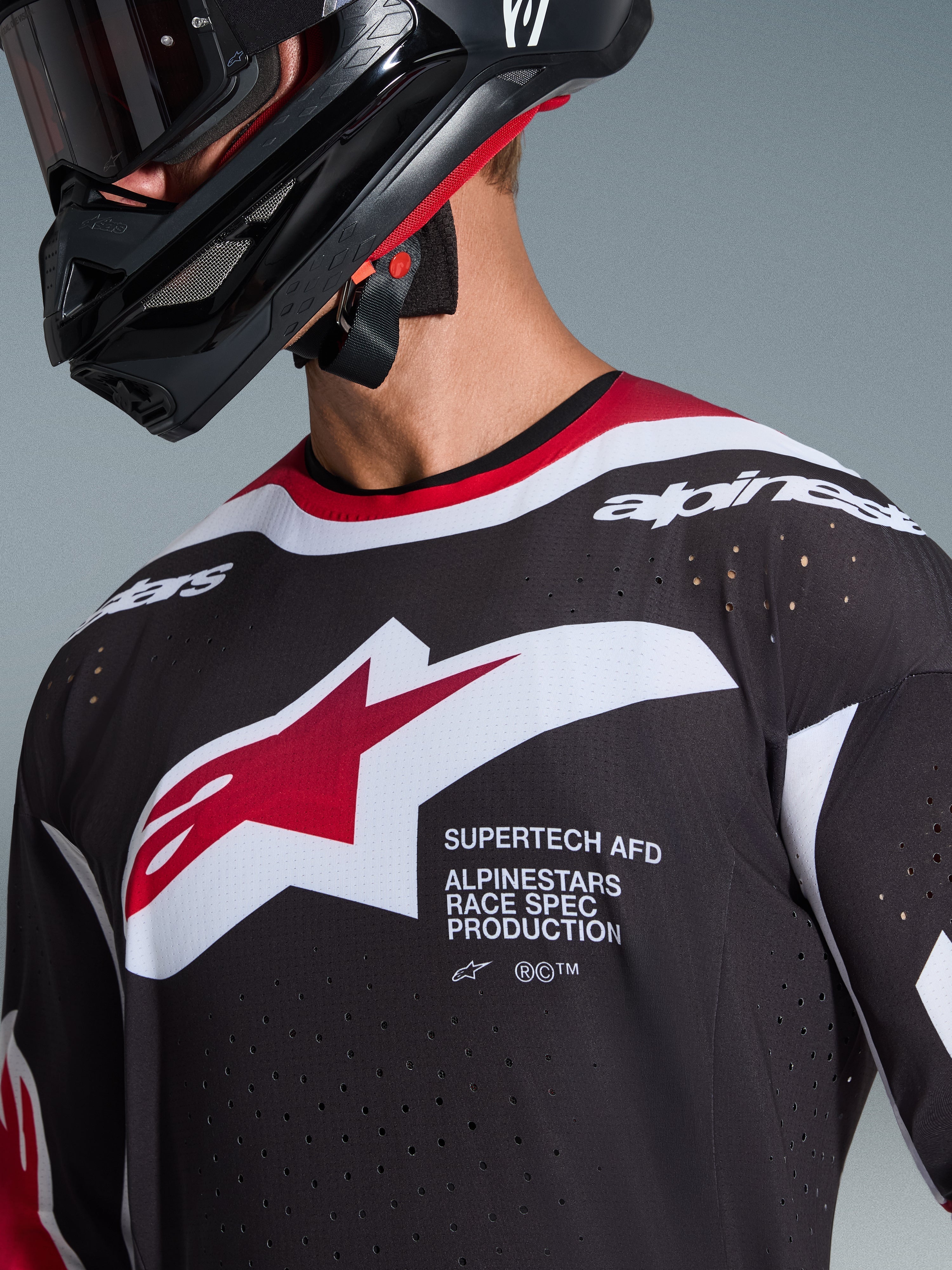 Alpinestars 2026 Supertech AFD Vista Jersey, Schwarz, Rot und Weiß, Nahaufnahme der Brust mit Alpinestars Stern-Logo und 'Supertech AFD' Schriftzug, lasergeschnittene Belüftungslöcher und Mesh-Konstruktion, getragen mit schwarzem Motocross-Helm.