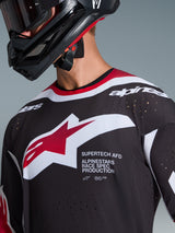 Alpinestars 2026 Supertech AFD Vista Jersey, close-up of a motocross rider wearing a black jersey with red and white accents, featuring a large white and red Alpinestars logo, laser-cut ventilation perforations, and professional racing fit, paired with a black helmet.