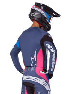 Motocross-Fahrer in der Rückansicht mit dem Alpinestars 2025 Techstar Dreem Ausrüstungsset in Grau, blaugraues Trikot und Hose mit pinken und schwarzen Einsätzen, weiße Alpinestars-Logos auf den Ärmeln und dem Rücken, passender schwarzer Helm mit blau-pinken Grafiken.