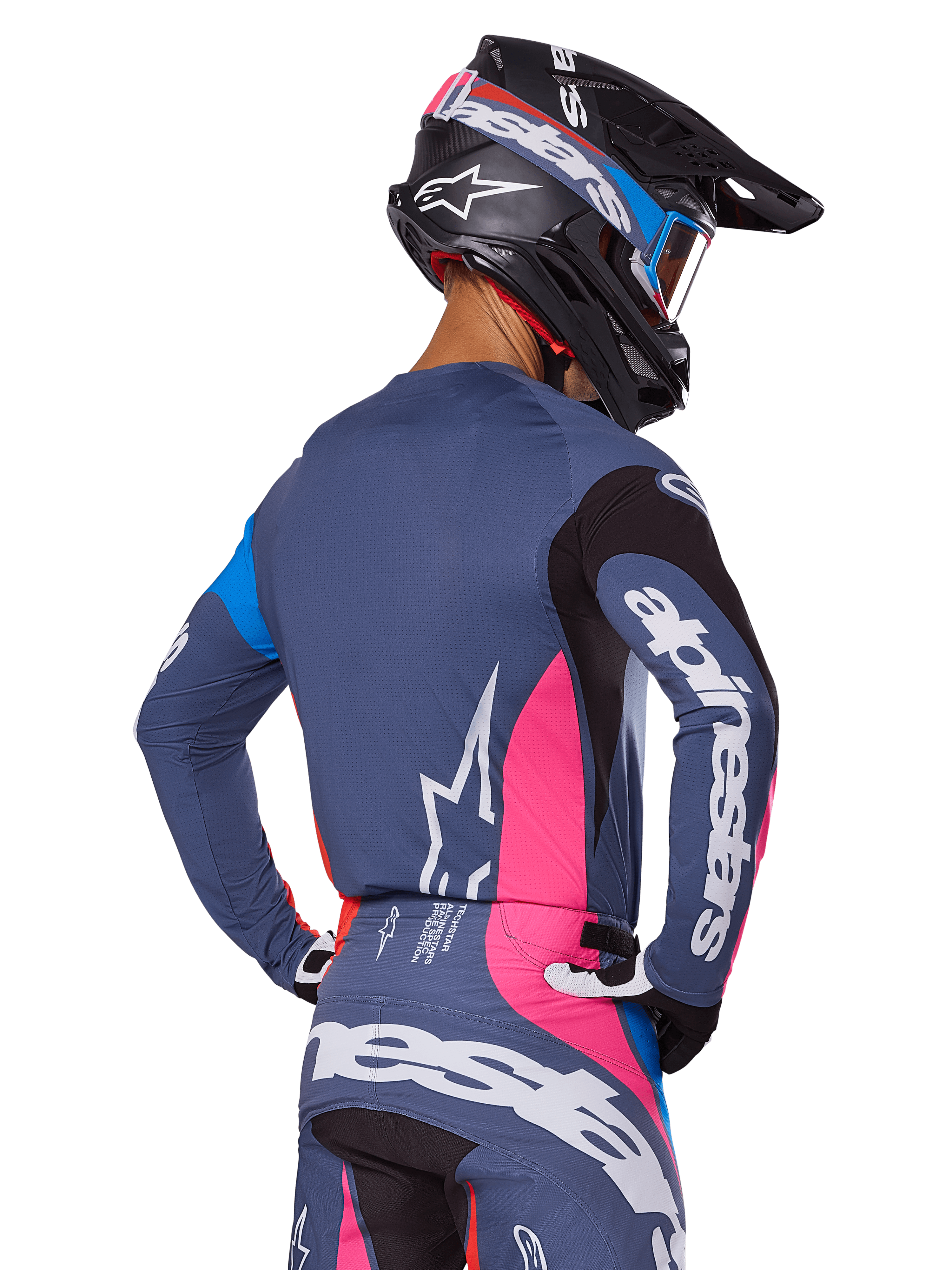 Motocross-Fahrer in der Rückansicht mit dem Alpinestars 2025 Techstar Dreem Ausrüstungsset in Grau, blaugraues Trikot und Hose mit pinken und schwarzen Einsätzen, weiße Alpinestars-Logos auf den Ärmeln und dem Rücken, passender schwarzer Helm mit blau-pinken Grafiken.