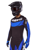 Motocross-Fahrer im Alpinestars 2025 Techstar Dreem Gear Set, schwarzes Jersey mit blauen Einsätzen im perforierten Stil und weißem Branding, passende schwarz-blaue Hose, schwarzer Rennhelm und blaue Handschuhe, abgestimmtes Performance-Outfit für Offroad-Motocross.