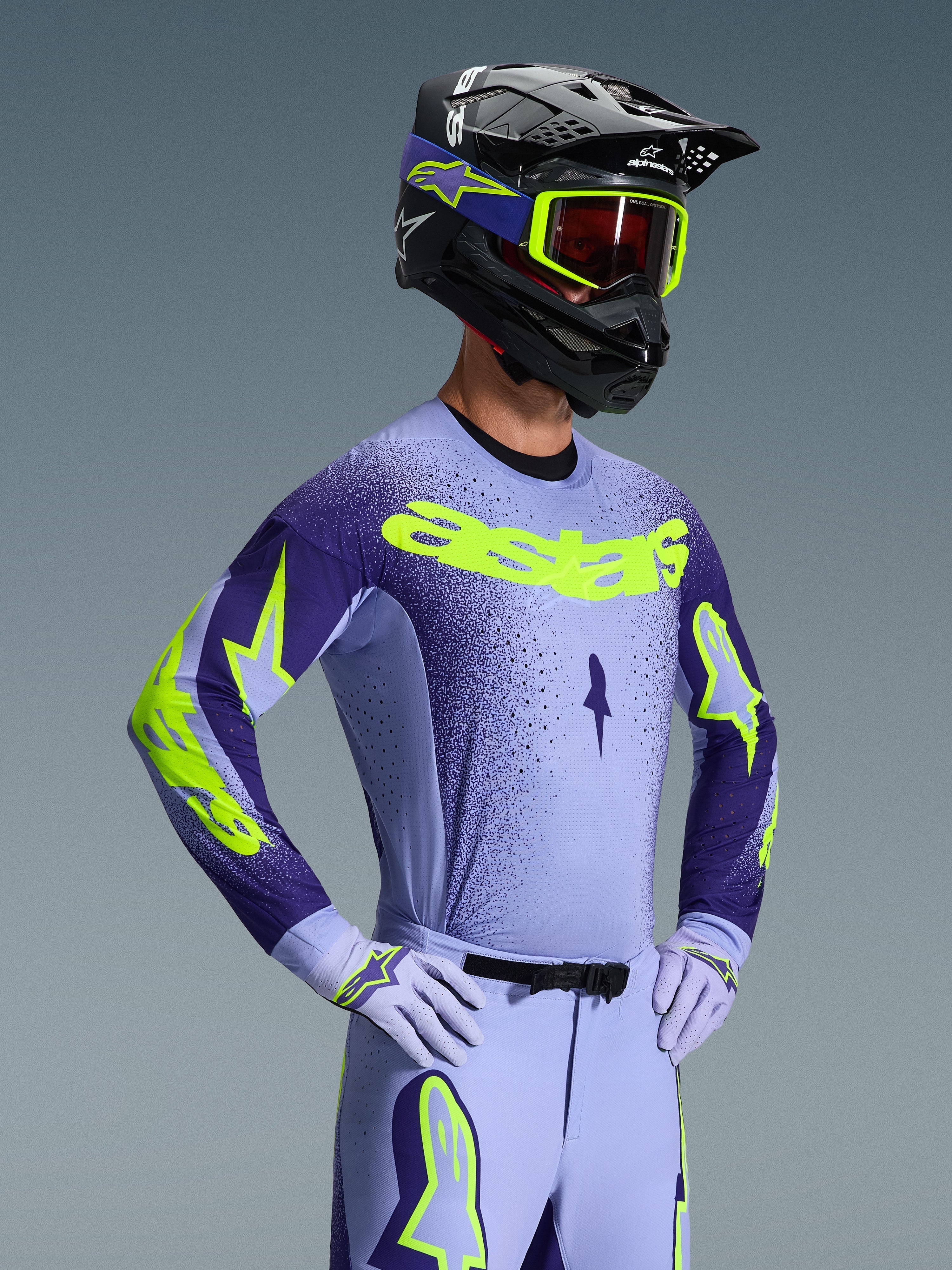 Motocross-Fahrer im 2026 Alpinestars Supertech Scenz Trikot, Lila und Gelb Fluo, passende lila Hose mit Fluo-Akzenten, schwarzer Helm mit gelber Brille und lila Rennhandschuhe, koordinierte Profi-Ausrüstung für den Offroad-Rennsport
