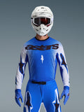 Alpinestars 2026 Supertech Scenz Jersey, Motocross-Rennoberteil, Ucla-Blau und Weiß, mit 'astars' Brust-Branding und Stern-Logos auf weißen Ärmeln, abgebildet mit passenden blauen Handschuhen und einem weißen Helm