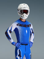 Alpinestars 2026 Supertech Scenz Trikot, Motocross-Trikot, Ucla Blue und Weiß, getragen als komplettes Ausrüstungsset mit passender blauer Hose und Handschuhen, mit schwarzem 'astars'-Branding, weißem Helm und dunkler Brille, professionelle athletische Rennpassform.