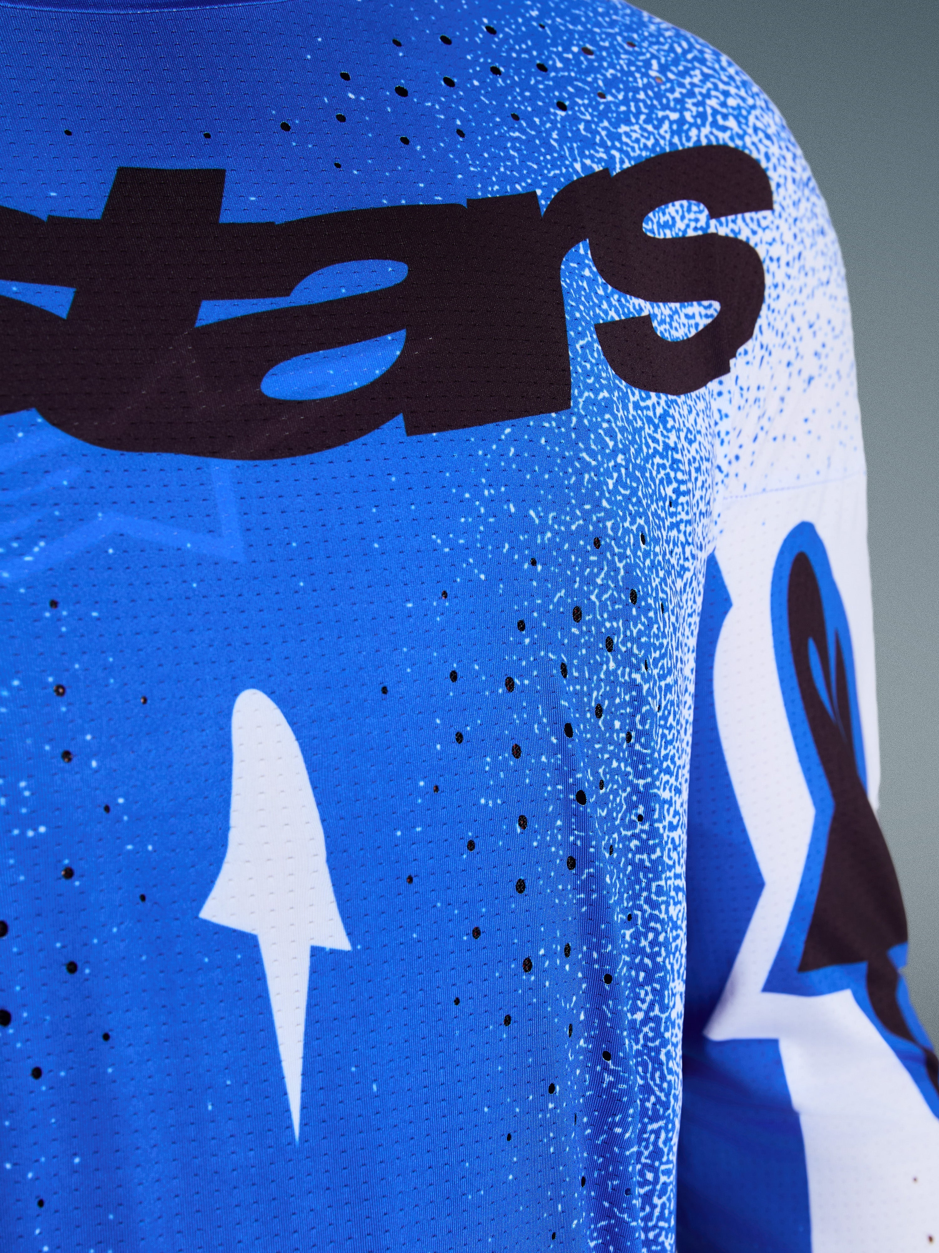Alpinestars 2026 Supertech Scenz Trikot, Nahaufnahme des Designs in Ucla Blau und Weiß, mit lasergeschnittenen Perforationen zur Belüftung, schwarzem 'stars' Branding und atmungsaktivem Mesh-Gewebe für professionellen Motocross-Rennsport.