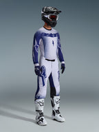 Motocross-Fahrer in kompletter professioneller Rennausrüstung, 2026 Supertech Scenz Trikot in Hellgrau und Dunkelblau, passende Motocross-Hose mit Stern-Grafiken, schwarzer Helm mit roter Brille, weiß-schwarze Performance-Stiefel, farblich abgestimmte blau-weiße Handschuhe für Offroad-Rennen
