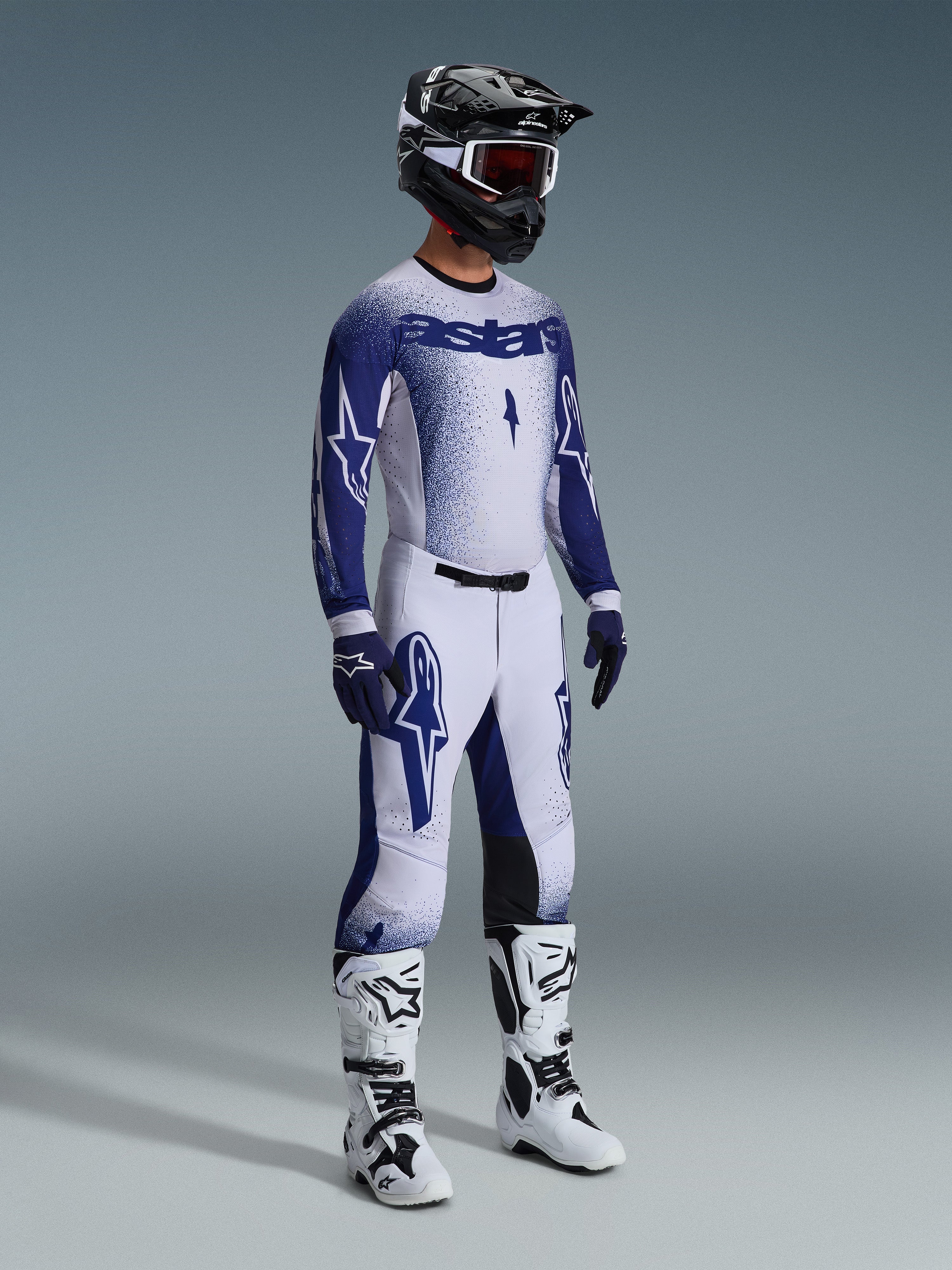 Alpinestars 2026 Supertech Scenz Gear Set, Motocross rider wearing white and navy blue racing jersey and pants with a gradient stipple effect, features bold Astars branding, paired with a black and white helmet, navy gloves, and white motocross boots.