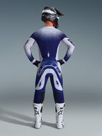 Motocross-Fahrer von hinten im Alpinestars 2026 Supertech Scenz Trikot, Hellgrau und Dunkelblau mit gepunktetem Farbverlauf-Design, passende Motocross-Hose, weiße Rennstiefel und schwarzer Helm, komplette Offroad-Rennausrüstung.