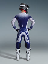 Motocross-Fahrer von hinten im Alpinestars 2026 Supertech Scenz Trikot, Hellgrau und Dunkelblau mit gepunktetem Farbverlauf-Design, passende Motocross-Hose, weiße Rennstiefel und schwarzer Helm, komplette Offroad-Rennausrüstung.