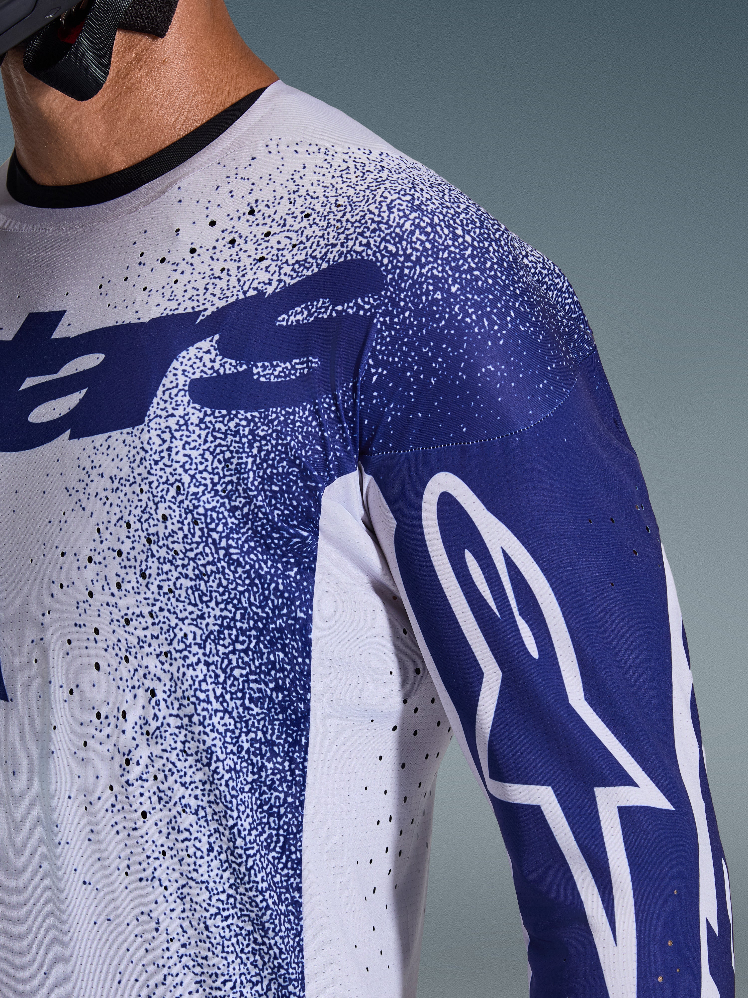 Nahaufnahme des Alpinestars 2026 Supertech Scenz Trikots in Hellgrau und Dunkelblau, mit lasergeschnittenen Perforationen, gesprenkeltem Grafikmuster, weißem Astars-Logo auf dem Ärmel, professionelle Motocross-Performance-Passform