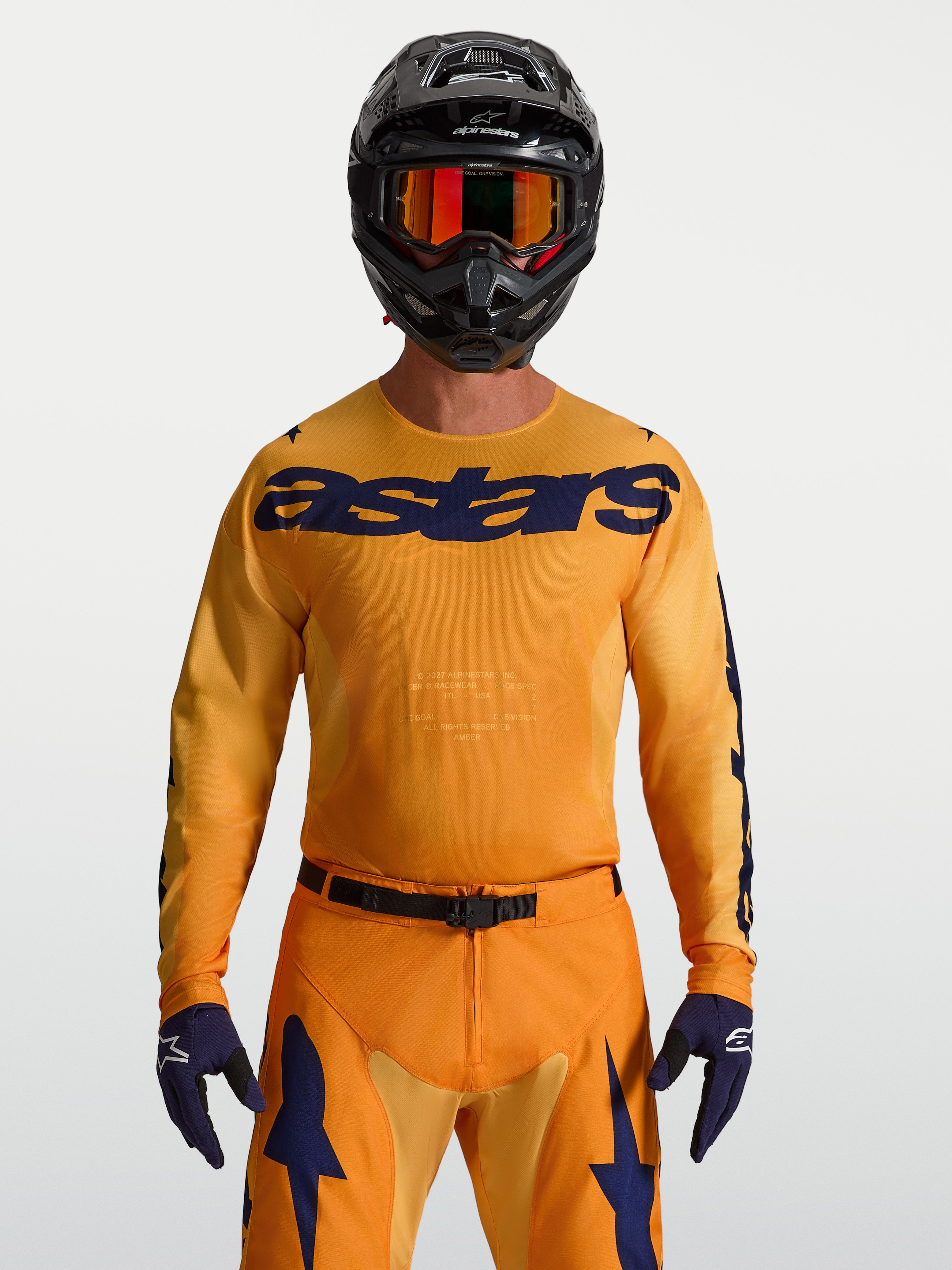 Alpinestars Racer Amber Trikot, Motocross-Renntrikot für Herren, Orange und Dunkelblau, feuchtigkeitsableitendes Material, getragen von einem Model mit Helm und Handschuhen.