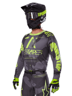 Alpinestars 2025 Racer Hollow Ausrüstungsset, Motocross-Jersey und -Hose in Grau und Neongelb, getragen mit passendem schwarzem Helm, Goggles und Handschuhen, mit markantem fluoreszierend gelbem Alpinestars-Branding und Stern-Grafiken auf einer gemusterten grauen Basis, koordinierter professioneller Offroad-Rennlook