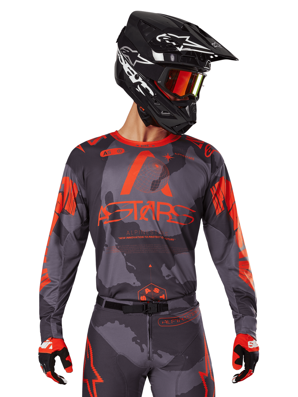 Alpinestars 2025 Racer Hollow Jersey, Motocross-Trikot, Gray Camo und Orange Fluo, getragen mit passendem Ausrüstungsset inklusive Hose und Handschuhen, schwarzer Helm mit weißen Grafiken und Schutzbrille, markantes ASTARS-Branding, schützende Offroad-Rennsportbekleidung