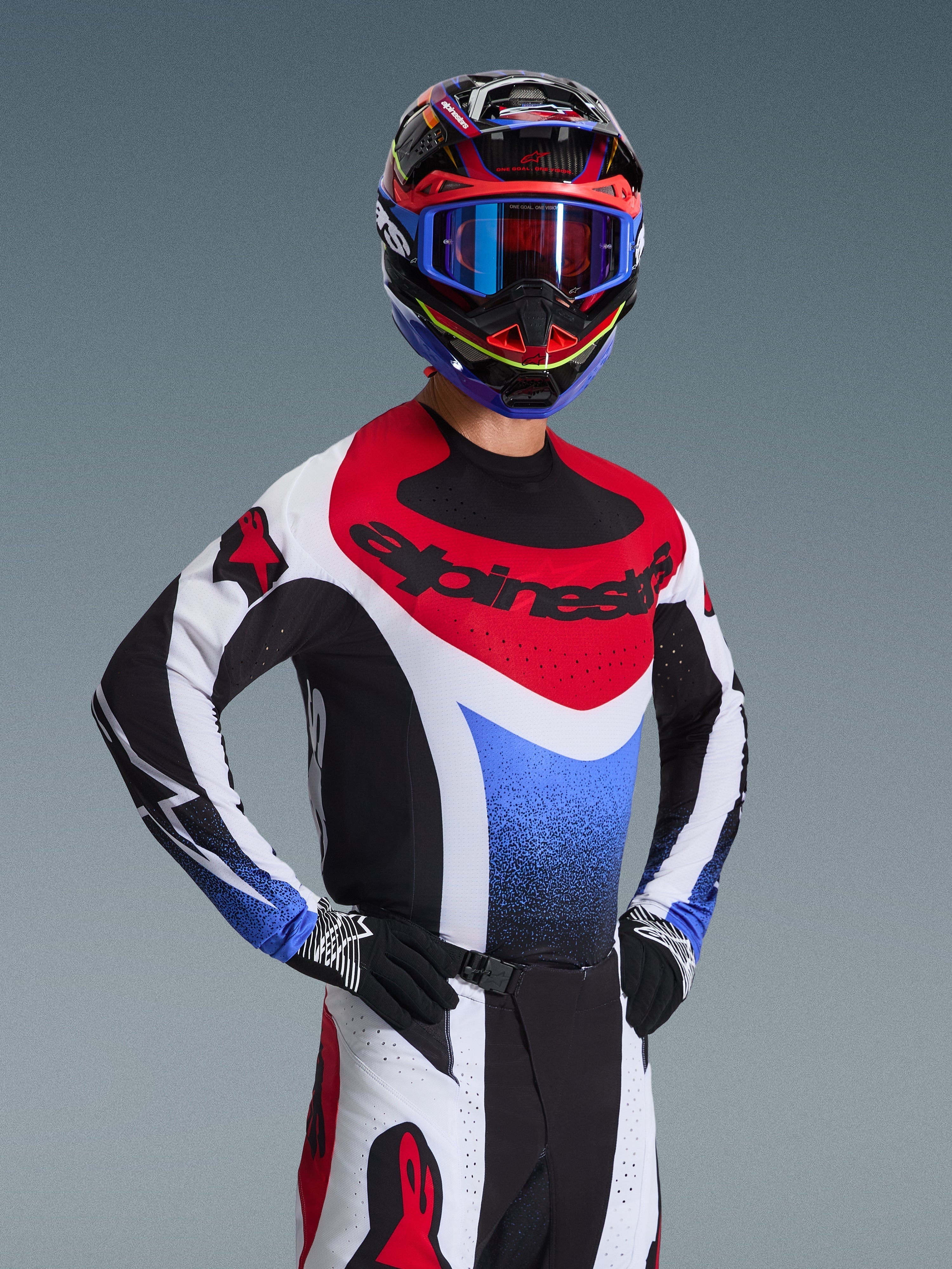 Motocross-Fahrer im Alpinestars 2026 Techstar Knif Trikot in Rot, Weiß und Blau, mit schwarzem Branding auf der Brust, passender Motocross-Hose, abgestimmtem Rennhelm mit blauer Brille und schwarz-weißen Handschuhen, professionelle Offroad-Ausrüstung für den Wettkampf