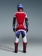 Alpinestars 2026 Techstar Knif Jersey, Motocross-Trikot, Schwarz, Weiß und Rot, Rückansicht eines Fahrers in passender Hose und Ausrüstung, leuchtend rote Rückenpartie, weiße Hose mit blauen Farbverläufen und rotem Branding, professionelle Offroad-Rennausrüstung