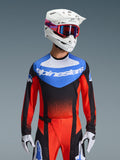 Alpinestars 2026 Techstar Knif Jersey, Motocross-Trikot, Orange, Schwarz und UCLA Blue, mit blauem Brusteinsatz, weißem Alpinestars-Logo und orange-roten Ärmeln, getragen mit weißem Helm, roter Brille und weißen Handschuhen, professionelle Offroad-Rennausrüstung